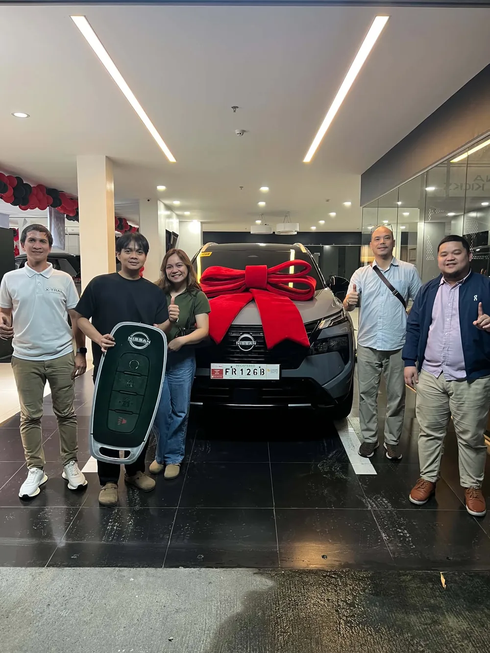 Customers and Nissan SVC Sucat staff beside a new Nissan with a red ribbon and oversized key