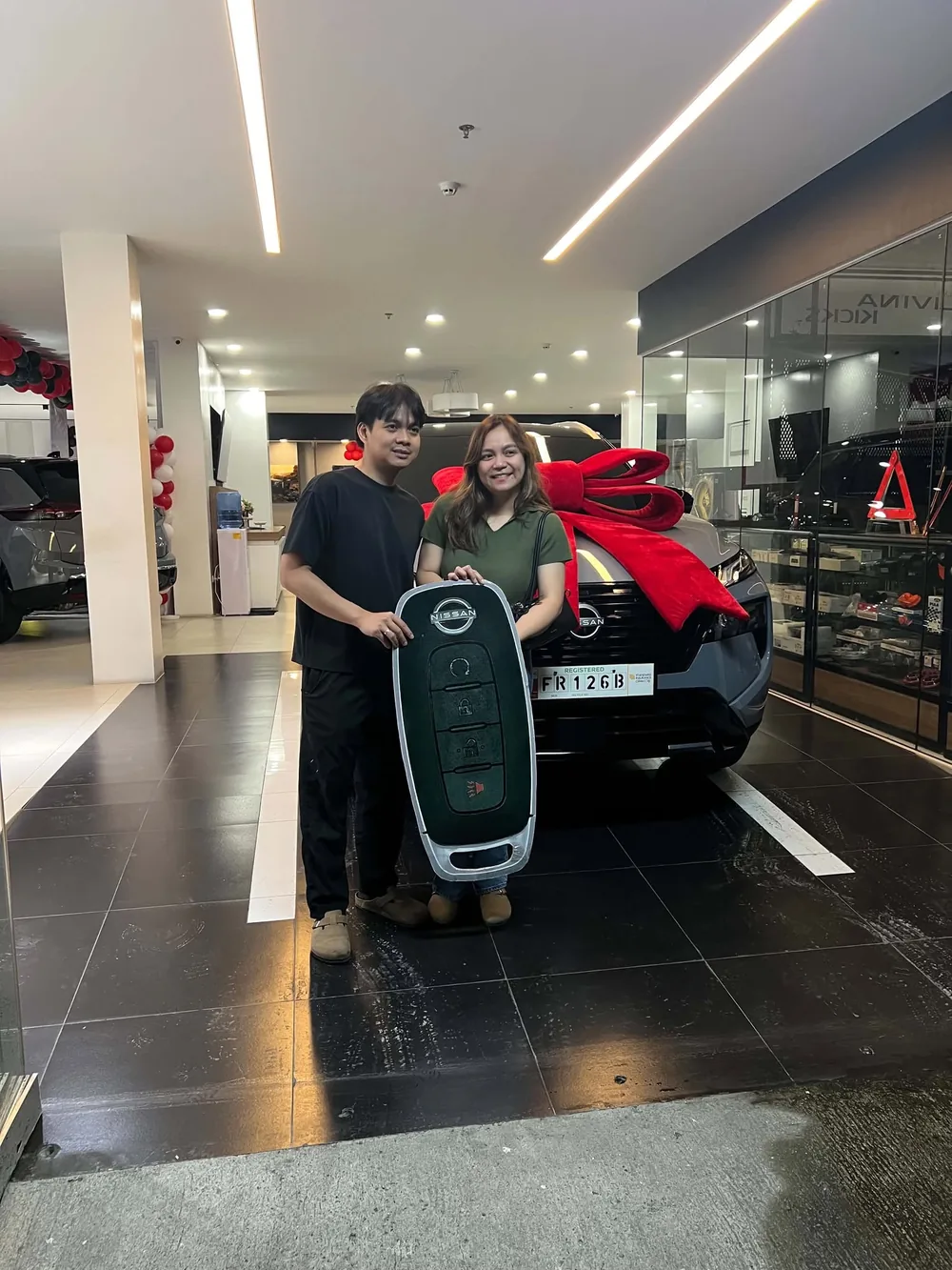 Two new owners holding the oversized key beside their ribboned Nissan